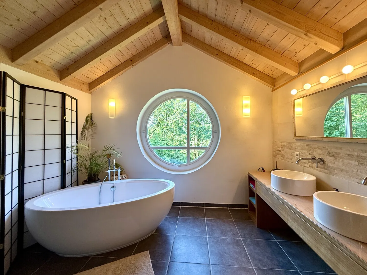 Großzügiges Wellnessbad mit freistehender Badewanne und markantem Rundfenster