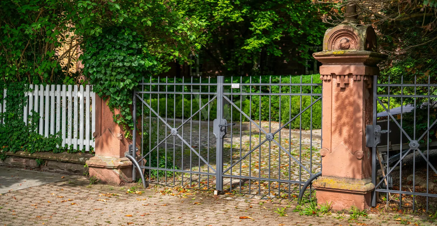 Schmiedeeisernes Eingangstor mit Sandsteinpfosten und begrünter Umgebung
