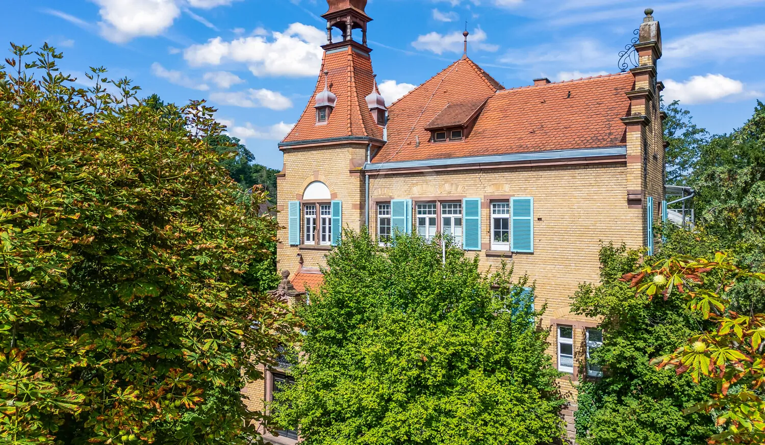Außenansicht des Gebäudes mit historischem Turm und rotem Ziegeldach