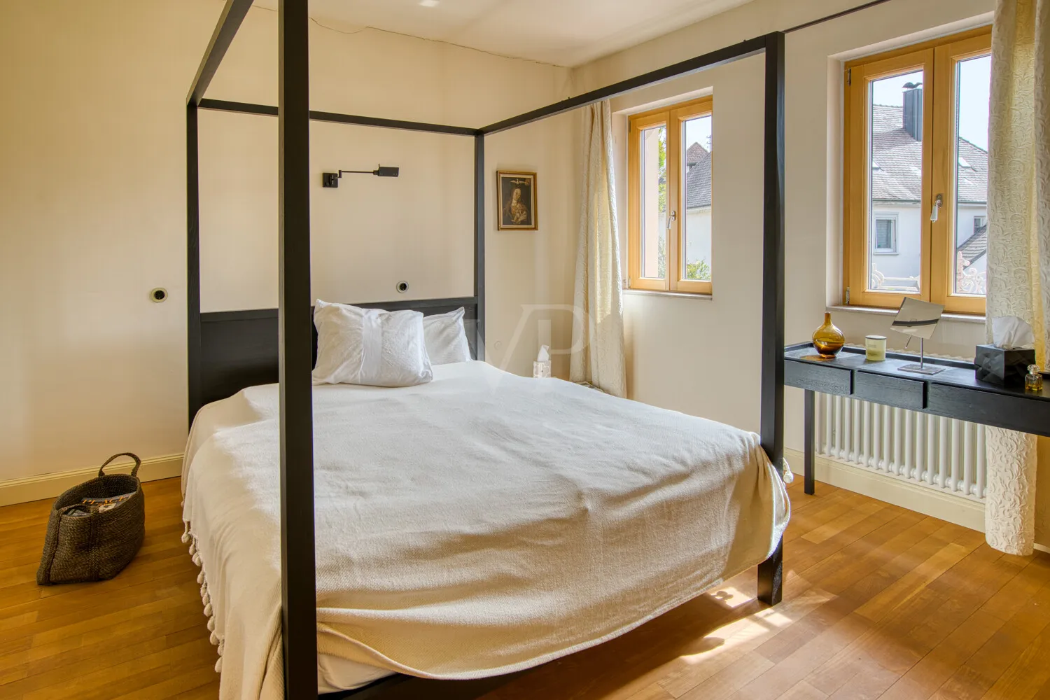 Schlafzimmer mit Parkettboden, gut belichtet durch zwei Fenster
