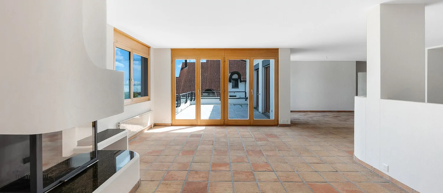 Open-plan Living mit Cheminée, grossen Fensterfronten und Zugang zur sonnigen Terrasse